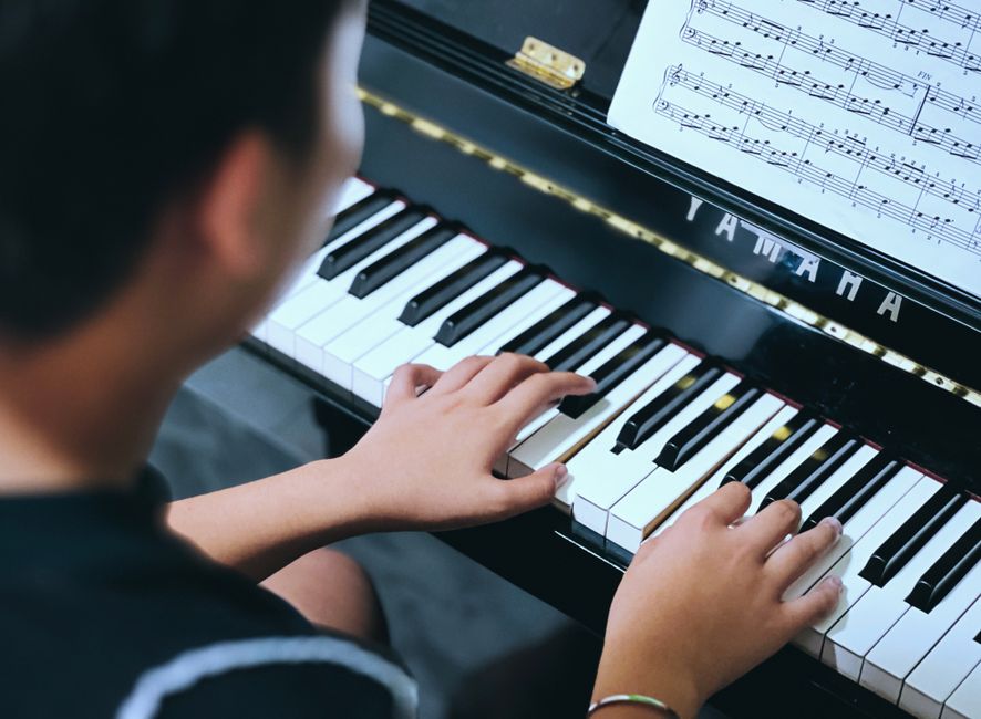 A young person playing piano with sheet music, focusing on musical creativity and skill.