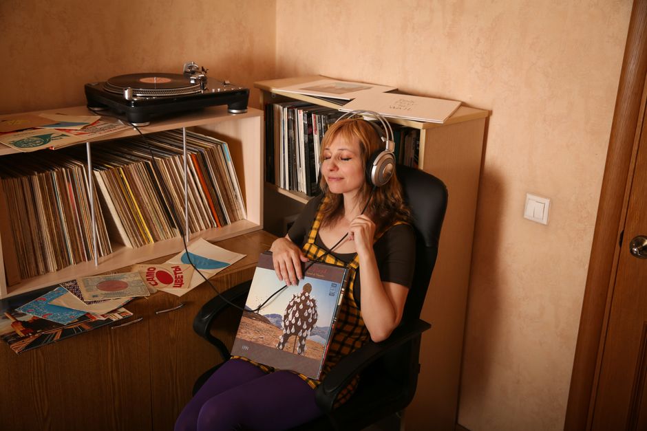 A woman with headphones enjoys vinyl records in a vintage room, surrounded by albums.