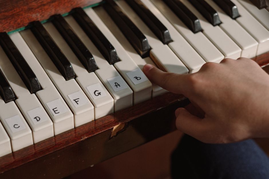 A person playing a labeled piano keyboard with finger pressing notes for learning music.